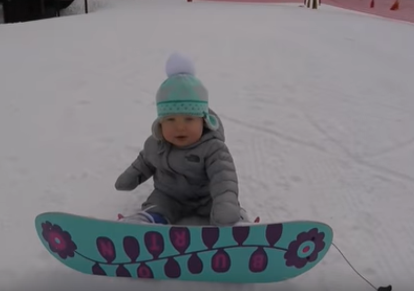 Момиченце на 1 година умело стои върху сноуборда 
